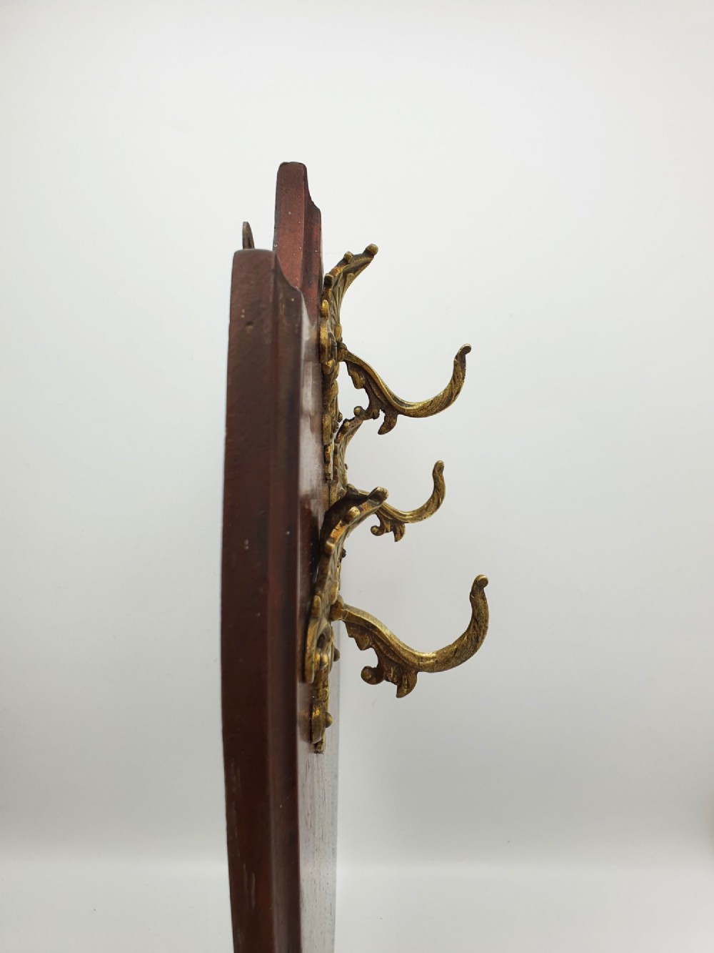 A shield-shaped mahogany wall plaque equipped with three decorative cast brass coat hooks arranged symmetrically. View VII