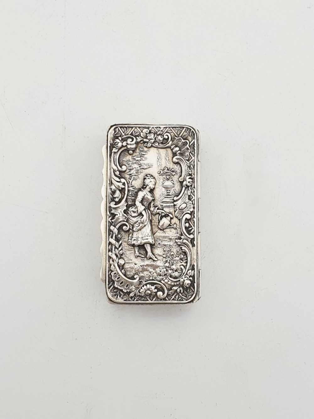 A rectangular Victorian sterling silver snuff box with intricate repousse relief work depicting a pastoral scene surrounded by floral scrollwork. View III