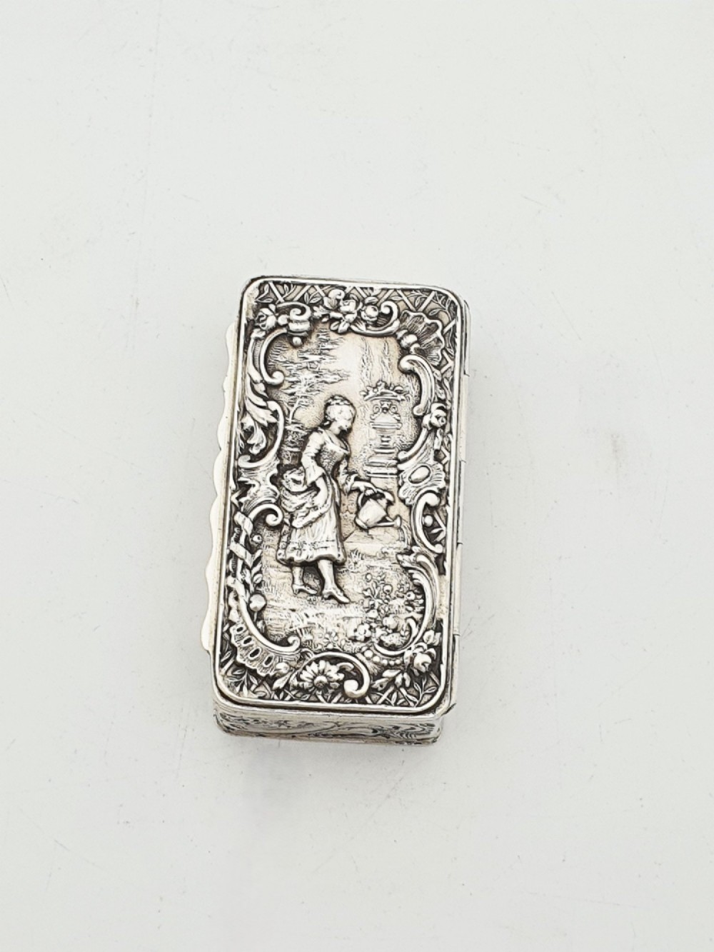 A rectangular Victorian sterling silver snuff box with intricate repousse relief work depicting a pastoral scene surrounded by floral scrollwork. View IV