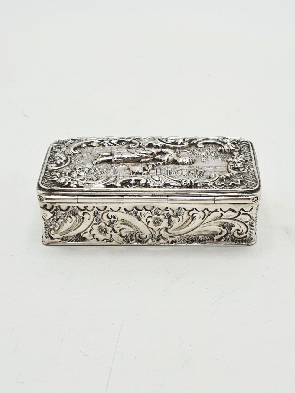 A rectangular Victorian sterling silver snuff box with intricate repousse relief work depicting a pastoral scene surrounded by floral scrollwork. View VI