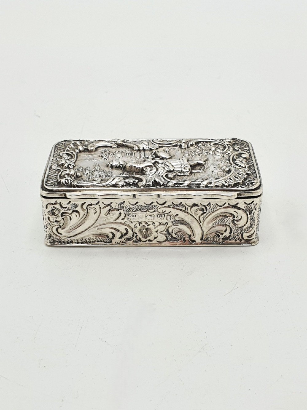A rectangular Victorian sterling silver snuff box with intricate repousse relief work depicting a pastoral scene surrounded by floral scrollwork. View VIII