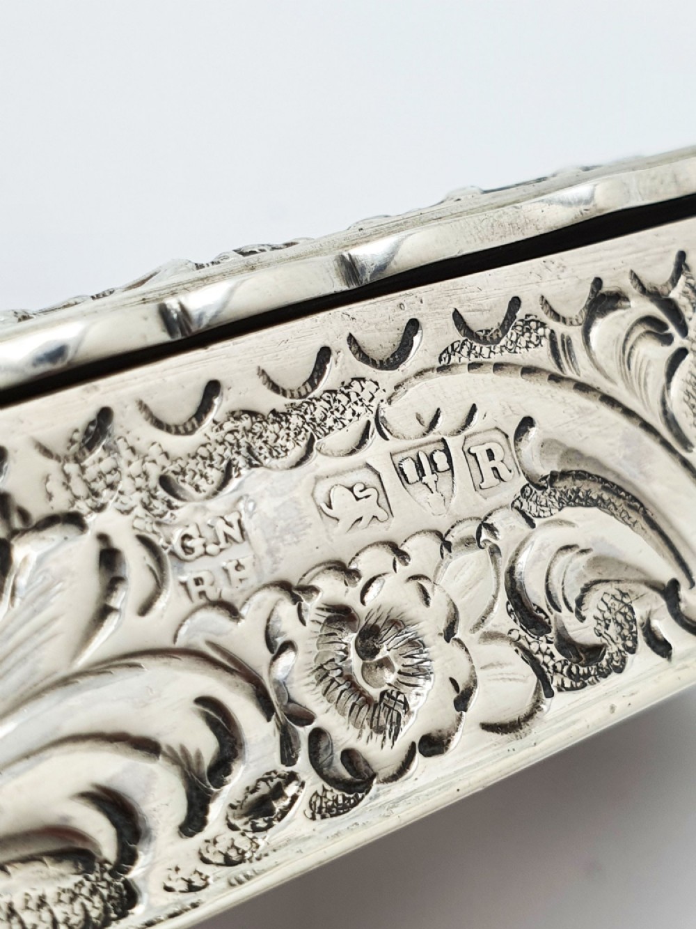A rectangular Victorian sterling silver snuff box with intricate repousse relief work depicting a pastoral scene surrounded by floral scrollwork. View IX