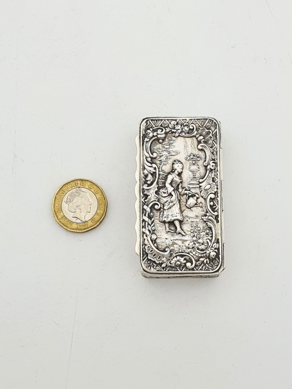 A rectangular Victorian sterling silver snuff box with intricate repousse relief work depicting a pastoral scene surrounded by floral scrollwork. View XI