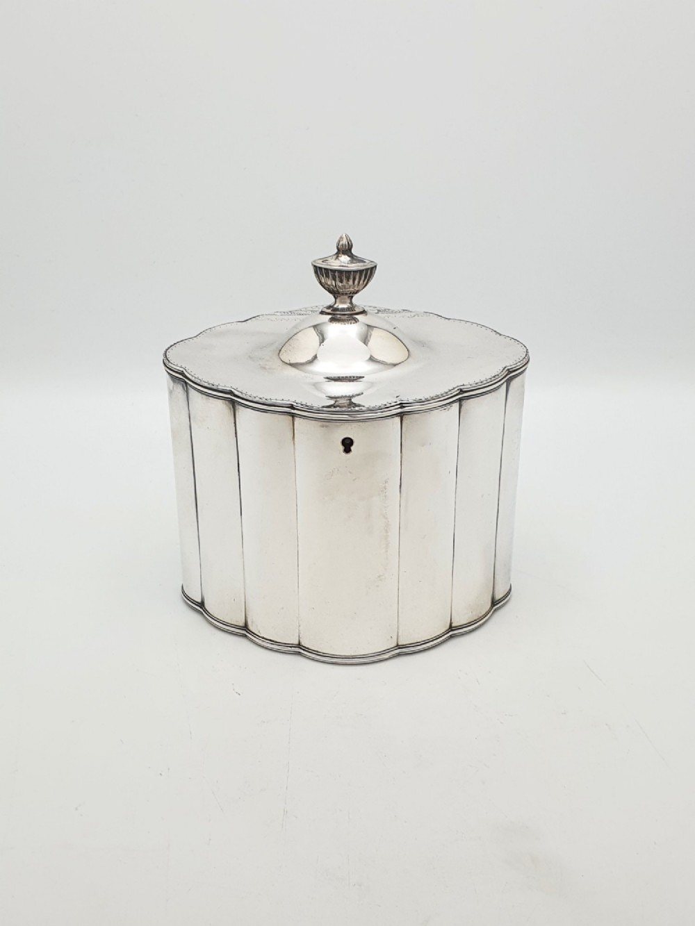 A lobed Georgian Sheffield plated tea caddy featuring vertical fluting, a central keyhole, and a domed lid topped with an urn finial.