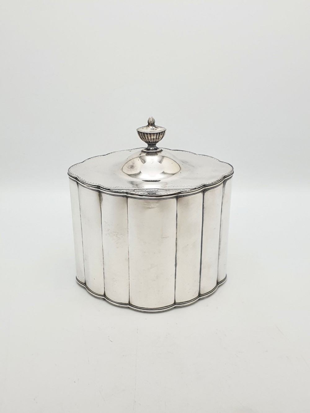 A lobed Georgian Sheffield plated tea caddy featuring vertical fluting, a central keyhole, and a domed lid topped with an urn finial. View V