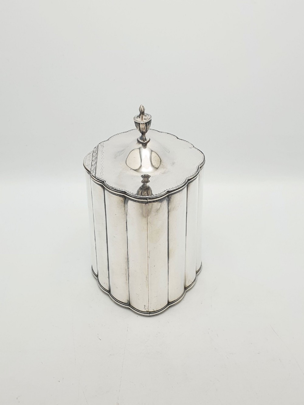 A lobed Georgian Sheffield plated tea caddy featuring vertical fluting, a central keyhole, and a domed lid topped with an urn finial. View VI