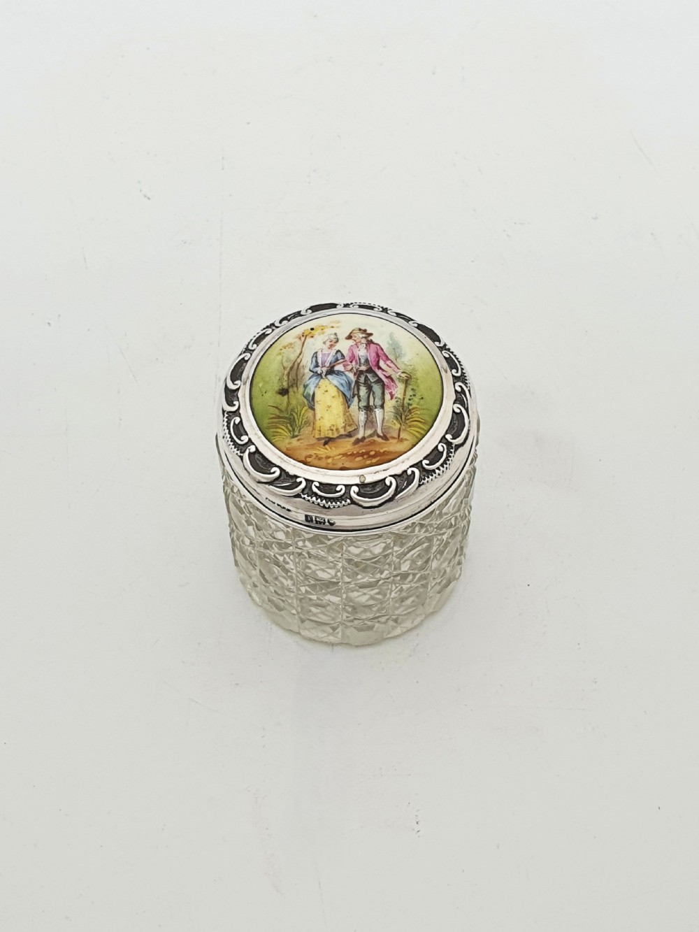 An Edwardian round cut-glass vanity jar featuring a sterling silver mounted lid inset with a hand-painted porcelain plaque depicting an eighteenth-century courting couple. View II