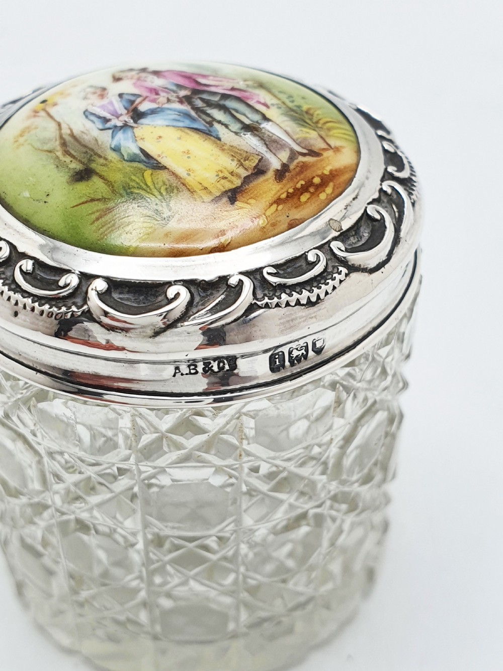 An Edwardian round cut-glass vanity jar featuring a sterling silver mounted lid inset with a hand-painted porcelain plaque depicting an eighteenth-century courting couple. View IV