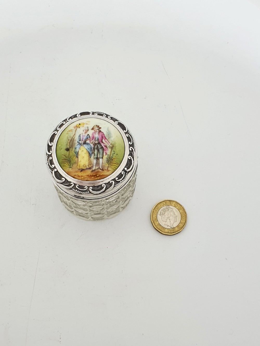 An Edwardian round cut-glass vanity jar featuring a sterling silver mounted lid inset with a hand-painted porcelain plaque depicting an eighteenth-century courting couple. View V
