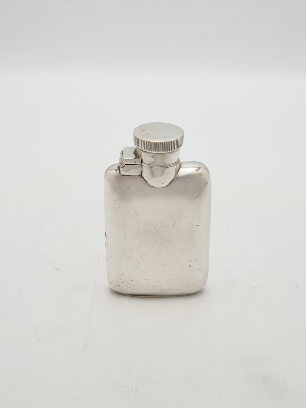 A small sterling silver rectangular hip flask with rounded corners and a hinged bayonet cap set against a plain white background.