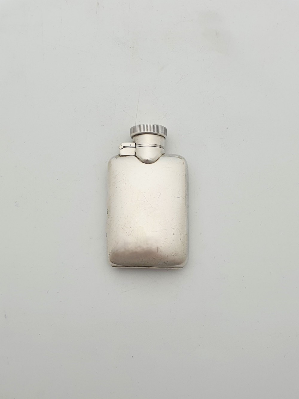 A small sterling silver rectangular hip flask with rounded corners and a hinged bayonet cap set against a plain white background. View III