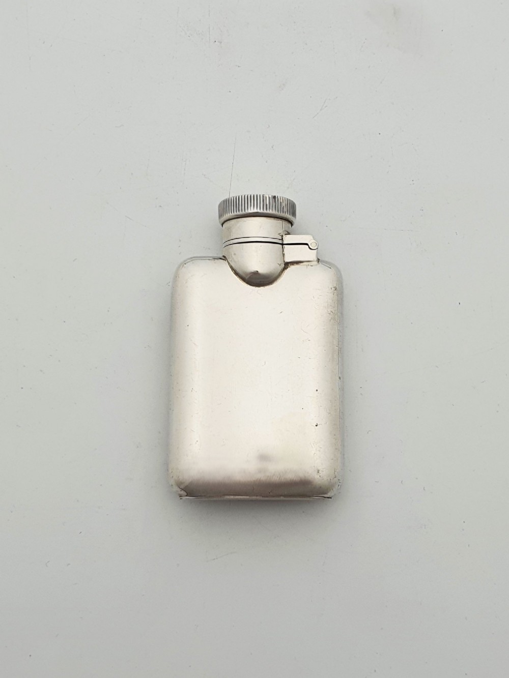 A small sterling silver rectangular hip flask with rounded corners and a hinged bayonet cap set against a plain white background. View IV