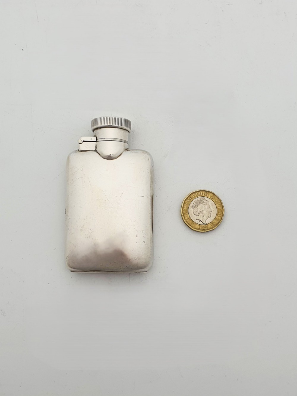 A small sterling silver rectangular hip flask with rounded corners and a hinged bayonet cap set against a plain white background. View VII