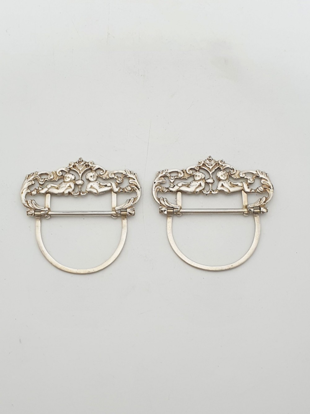 A pair of Victorian sterling silver place card holders featuring detailed cherubs framed by pierced scrolling foliage. View VI