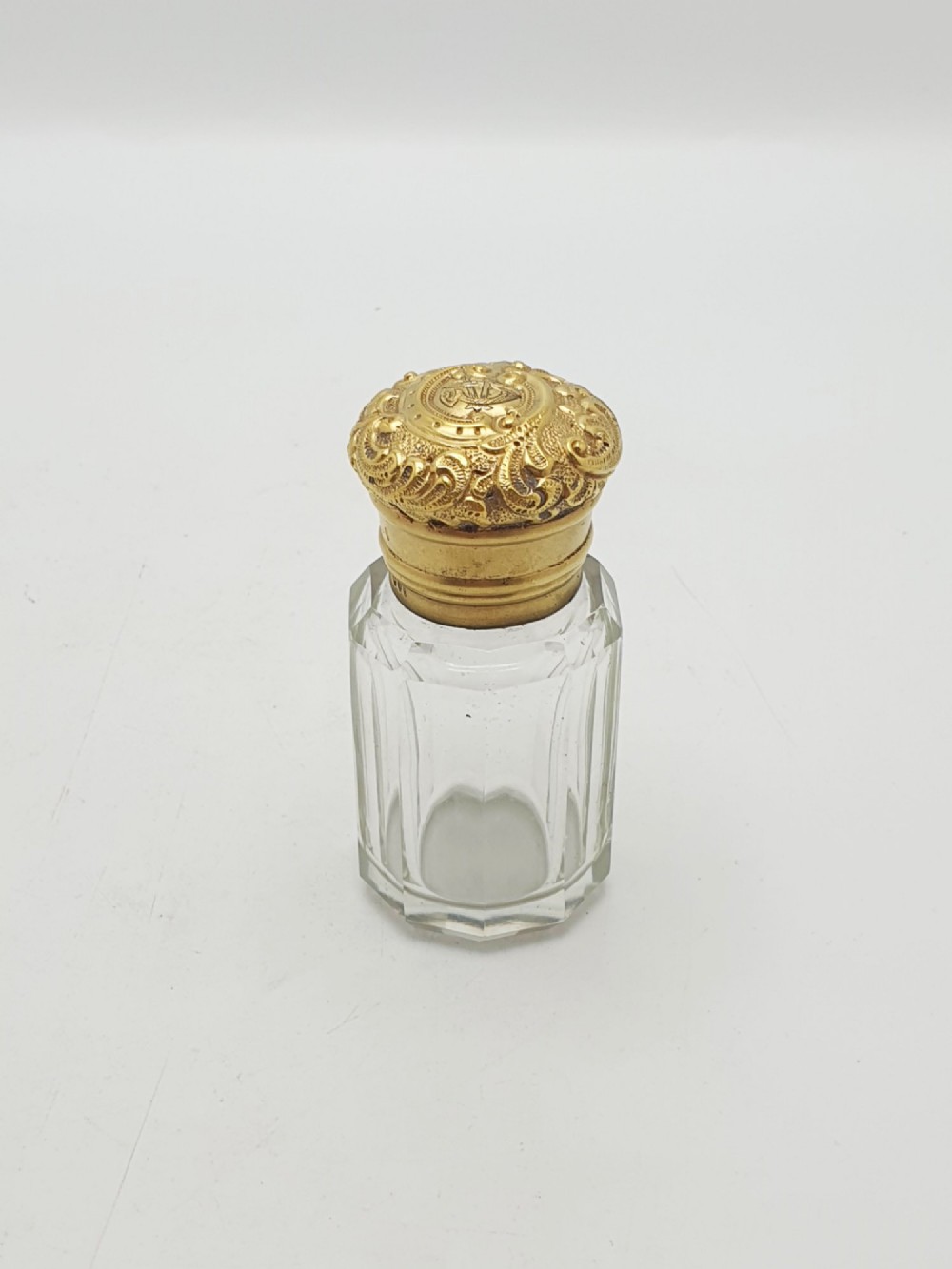 A clear faceted cut glass scent bottle featuring an embossed gilt sterling silver cap.