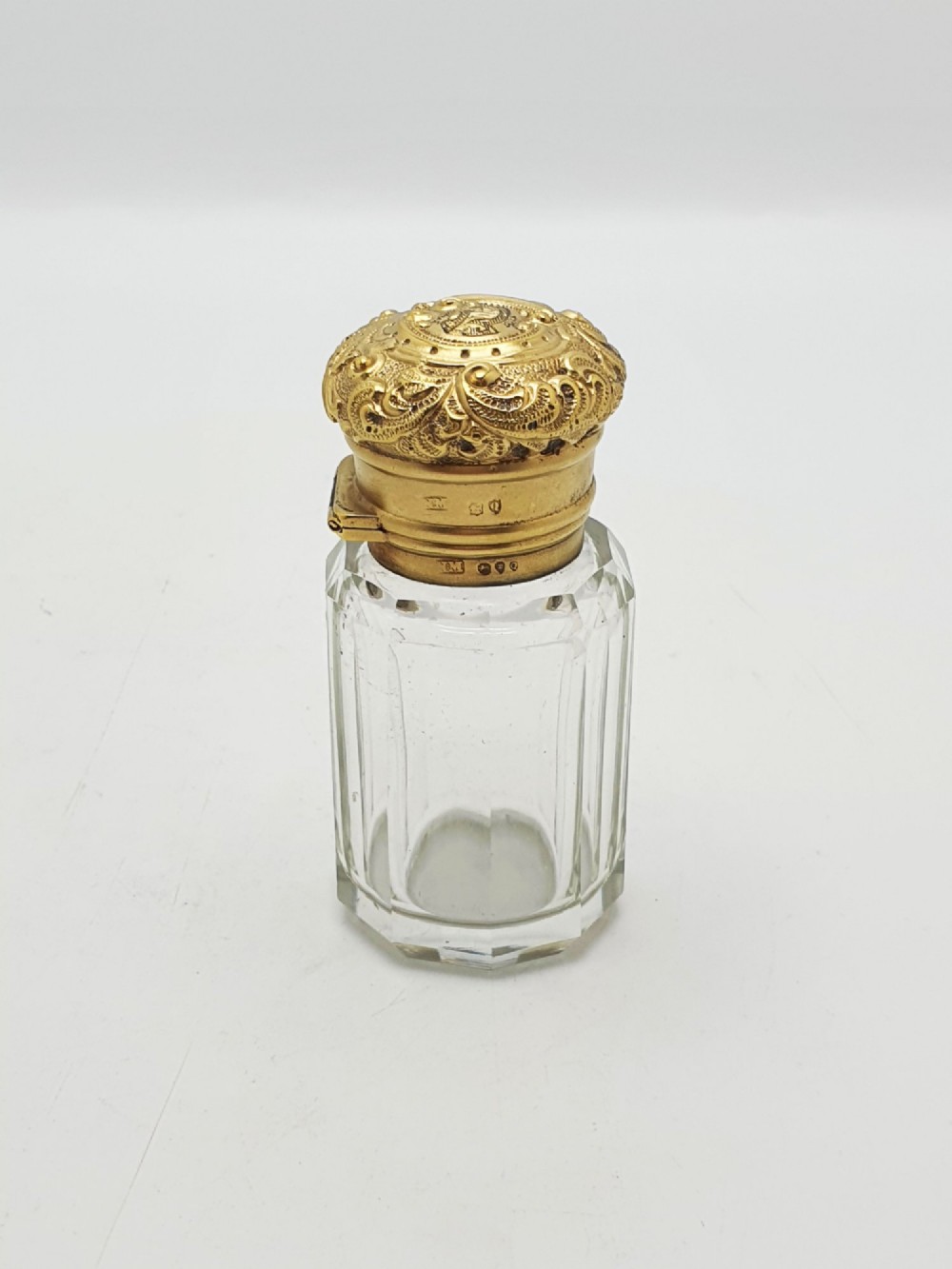 A clear faceted cut glass scent bottle featuring an embossed gilt sterling silver cap. View VII