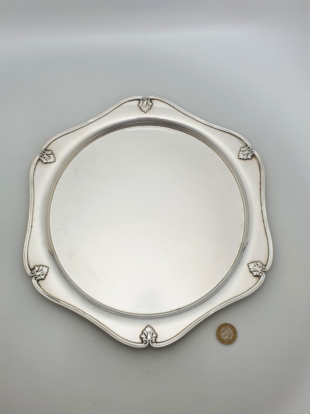 An Art Deco silver-plated circular cocktail tray featuring a scalloped rim decorated with stylised leaf motifs. View V