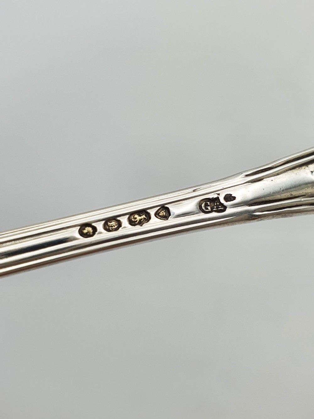 An antique sterling silver Kings pattern condiment spoon featuring a relief shell motif handle and a small rounded bowl. View III