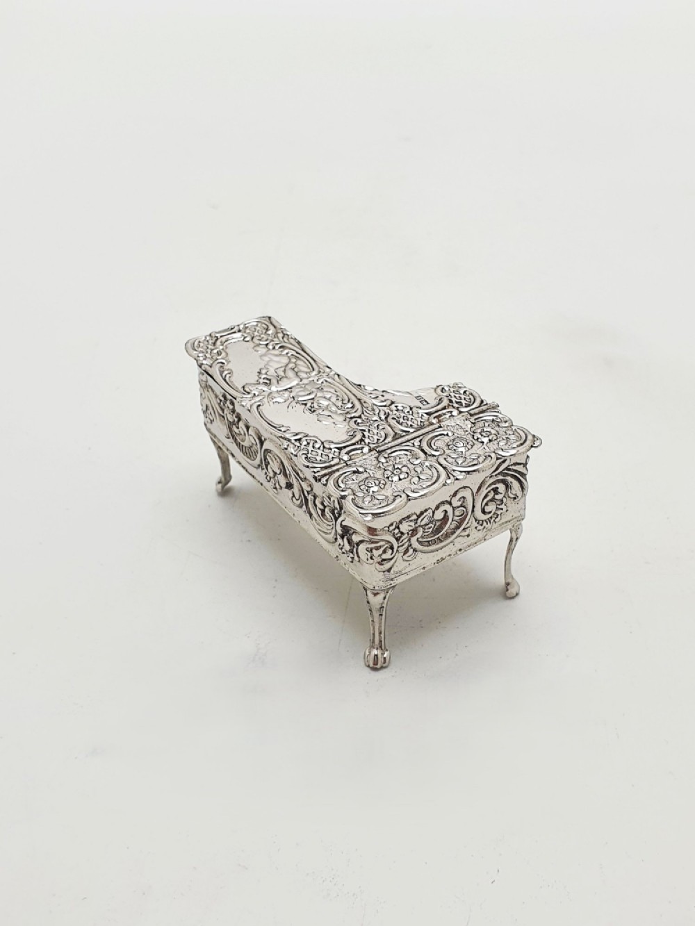 A miniature sterling silver trinket box shaped like a grand piano with embossed cherub motifs and cabriole legs.
