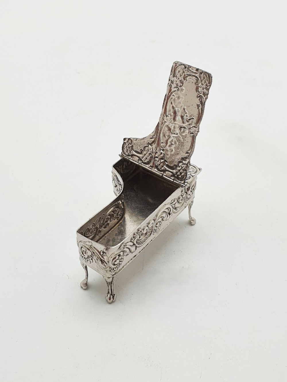 A miniature sterling silver trinket box shaped like a grand piano with embossed cherub motifs and cabriole legs. View III