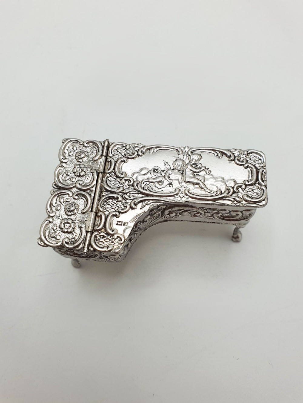 A miniature sterling silver trinket box shaped like a grand piano with embossed cherub motifs and cabriole legs. View VI