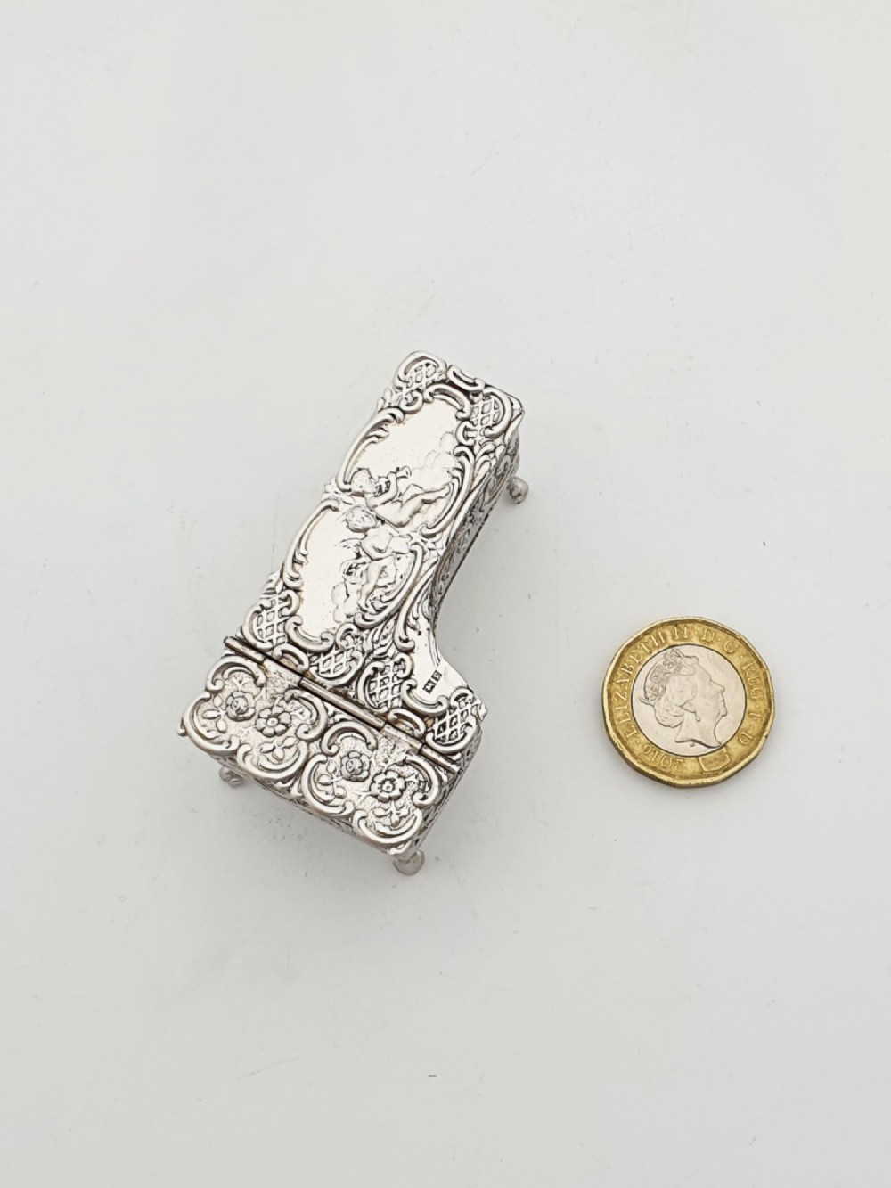 A miniature sterling silver trinket box shaped like a grand piano with embossed cherub motifs and cabriole legs. View VII
