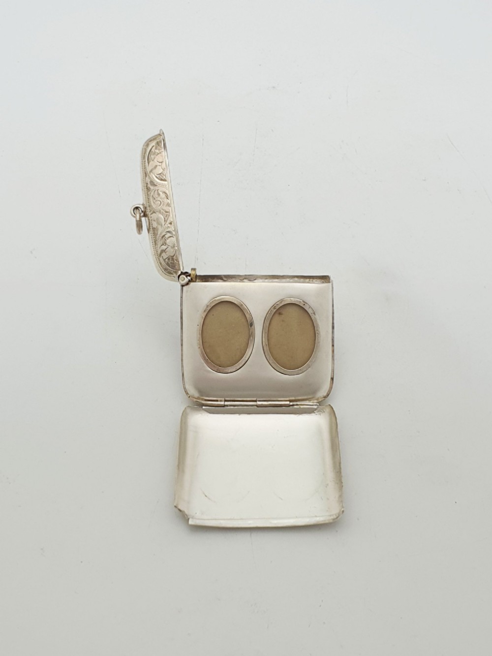 An open Edwardian sterling silver vesta case displaying an engraved hinged lid and two interior oval photo frame apertures.