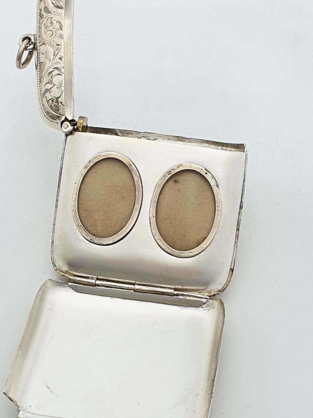 An open Edwardian sterling silver vesta case displaying an engraved hinged lid and two interior oval photo frame apertures. View V