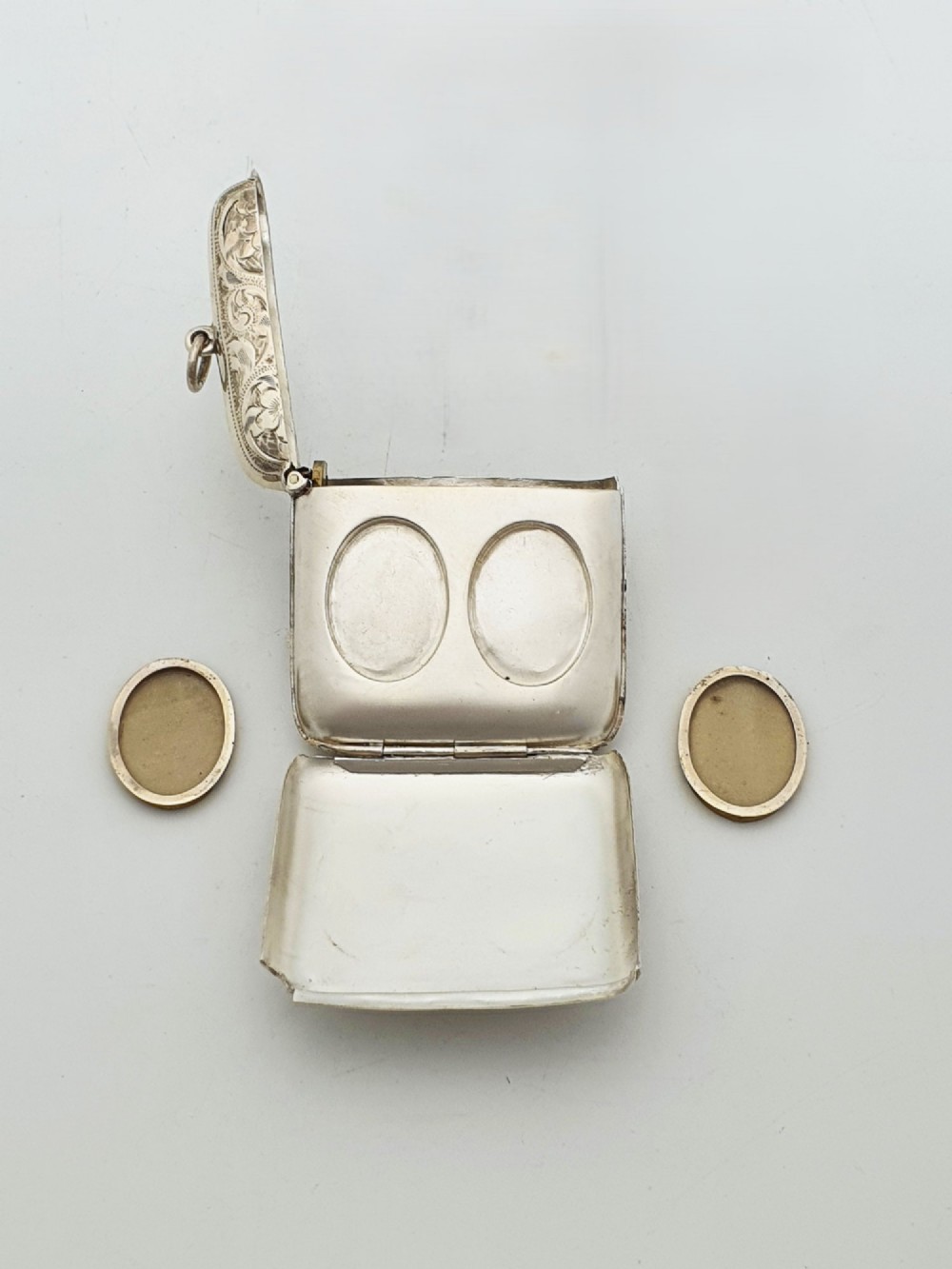 An open Edwardian sterling silver vesta case displaying an engraved hinged lid and two interior oval photo frame apertures. View VI