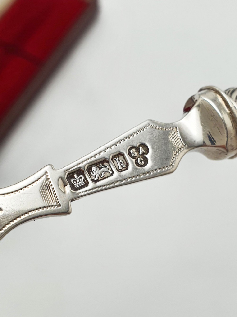 An Edwardian sterling silver bread fork featuring pierced foliage tines and a carved mother-of-pearl handle resting inside a red fitted box. View VI