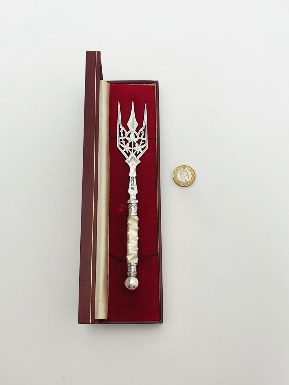 An Edwardian sterling silver bread fork featuring pierced foliage tines and a carved mother-of-pearl handle resting inside a red fitted box. View VII