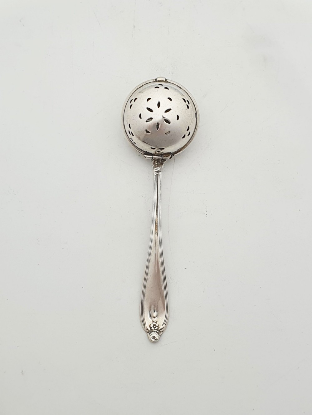 A George V sterling silver hinged tea infuser spoon featuring a perforated spherical bowl attached to a decorated handle. View III