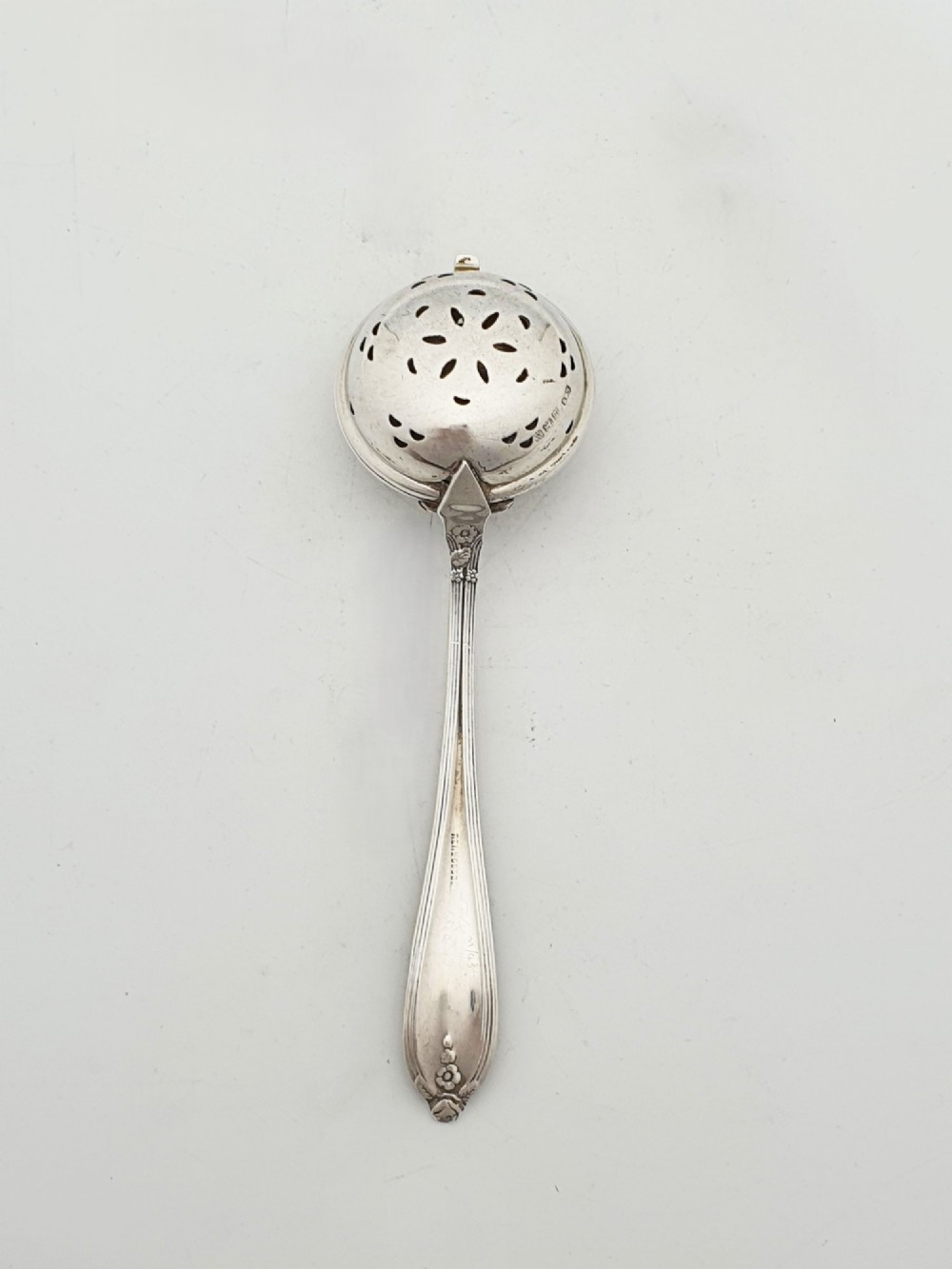A George V sterling silver hinged tea infuser spoon featuring a perforated spherical bowl attached to a decorated handle. View V