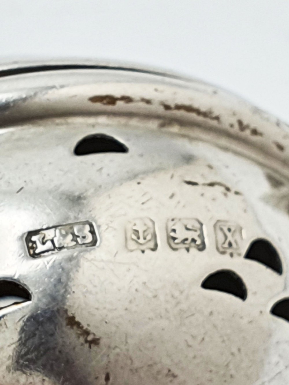 A George V sterling silver hinged tea infuser spoon featuring a perforated spherical bowl attached to a decorated handle. View VI