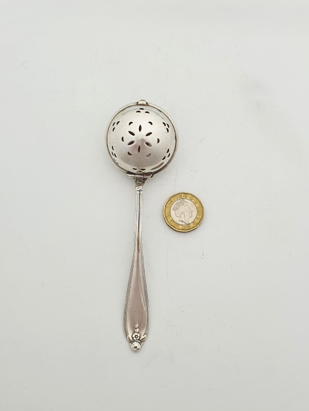 A George V sterling silver hinged tea infuser spoon featuring a perforated spherical bowl attached to a decorated handle. View VII
