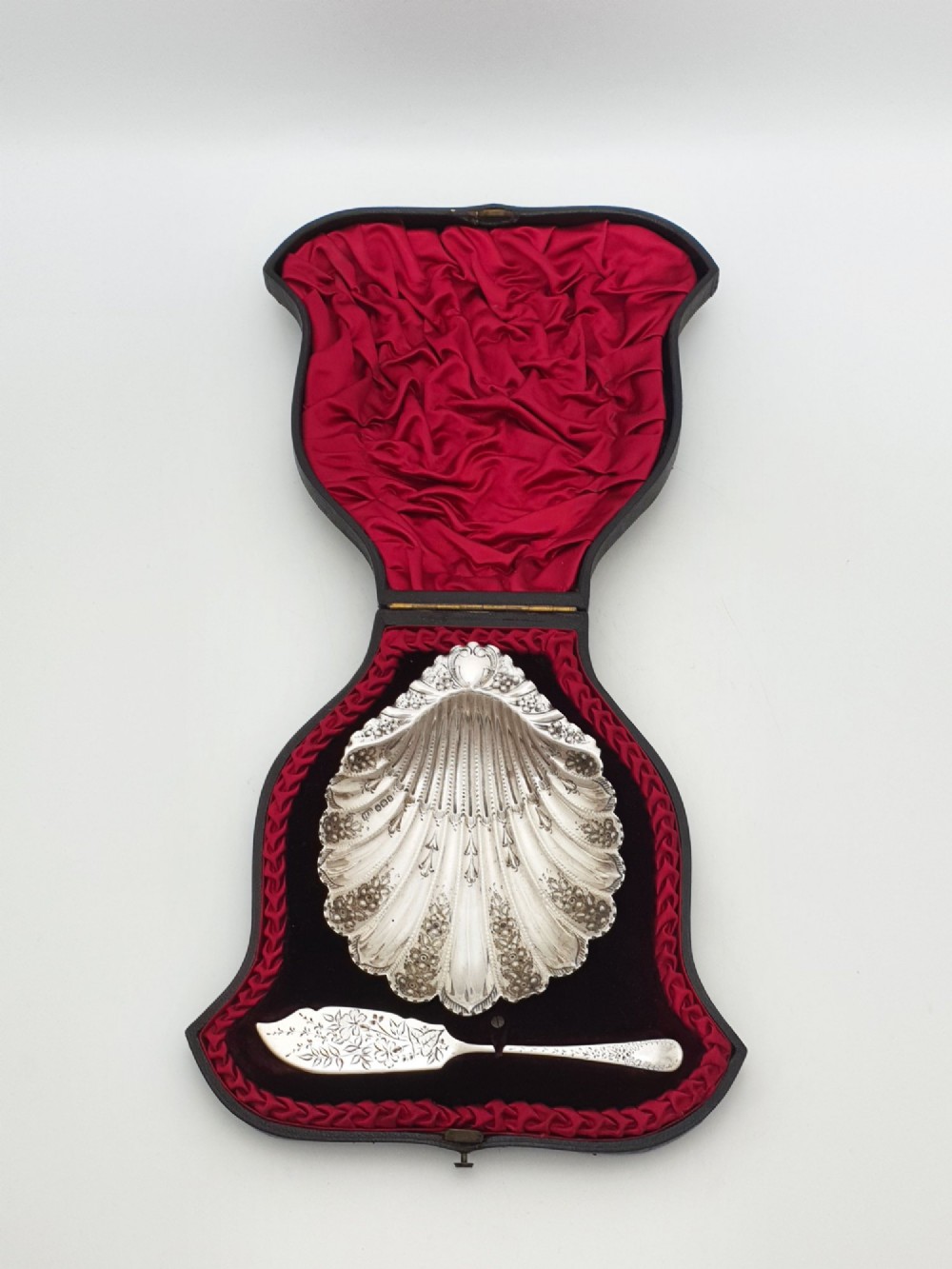 A Victorian sterling silver scallop shell butter dish and matching engraved spreader knife resting inside a fitted red and black velvet presentation case. View II