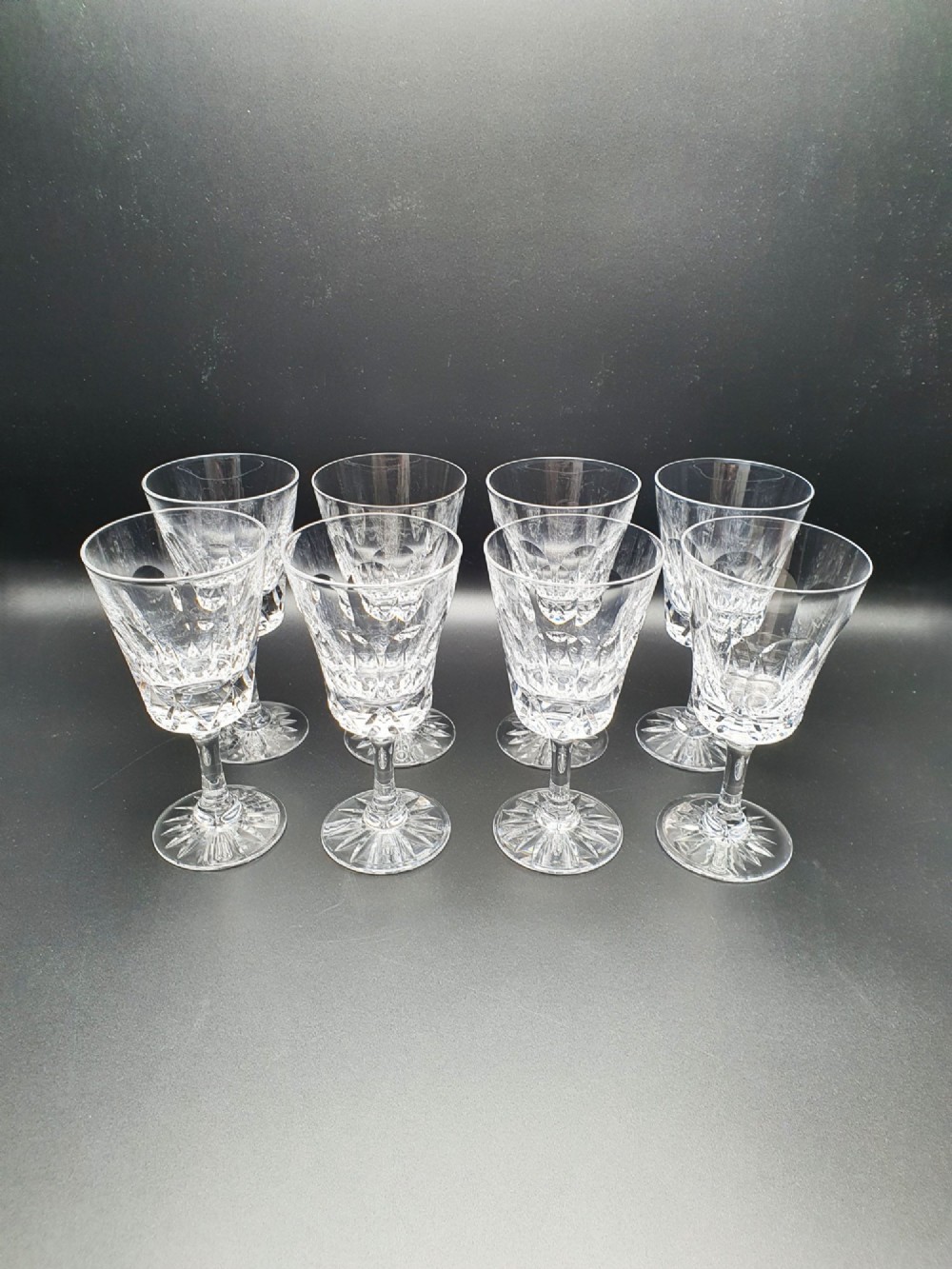 A set of eight clear cut glass wine glasses featuring faceted bowls and starburst pattern bases.