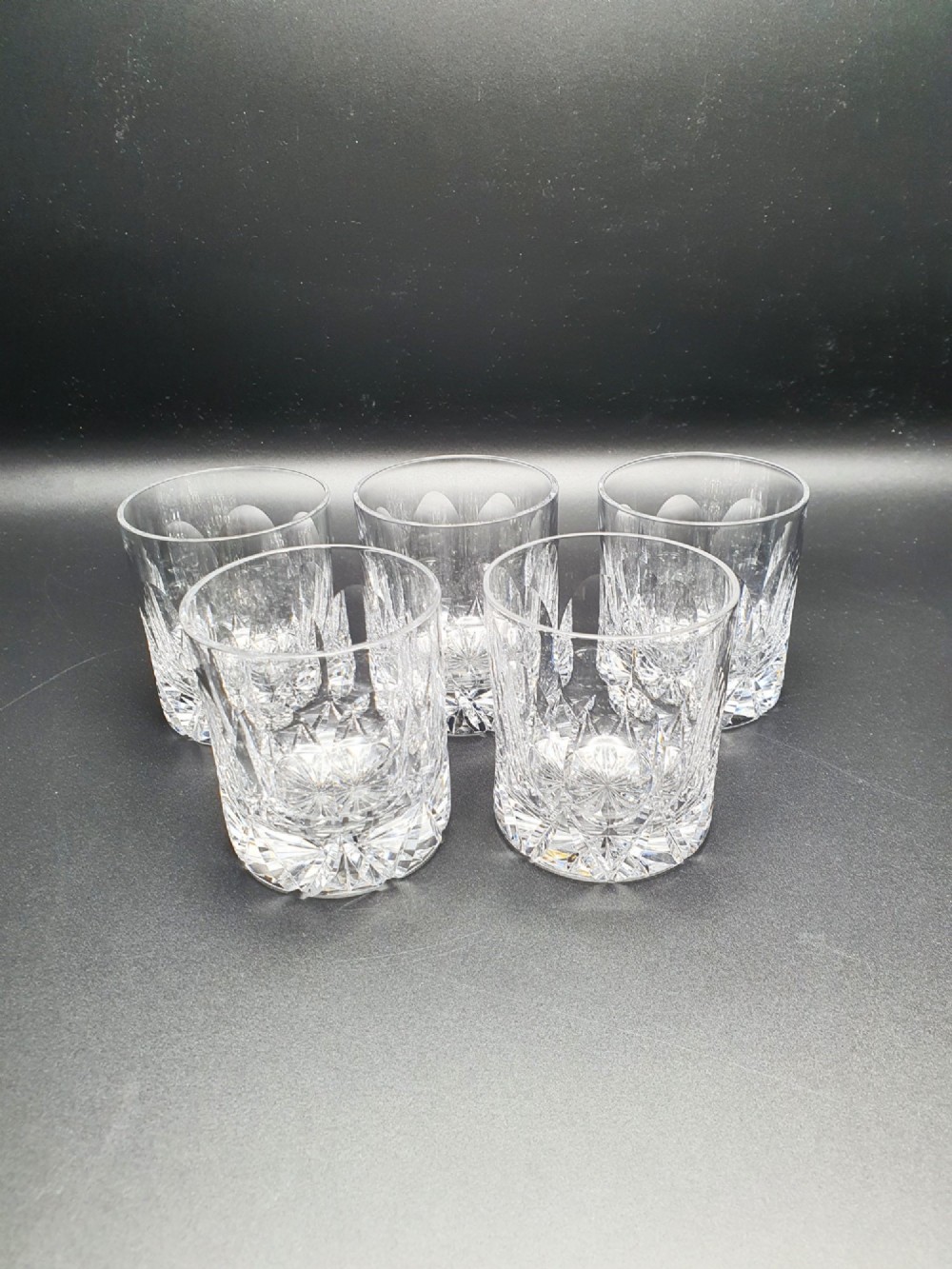 A set of five clear cut-glass tumblers featuring intricate geometric facet carvings around the lower half and base.
