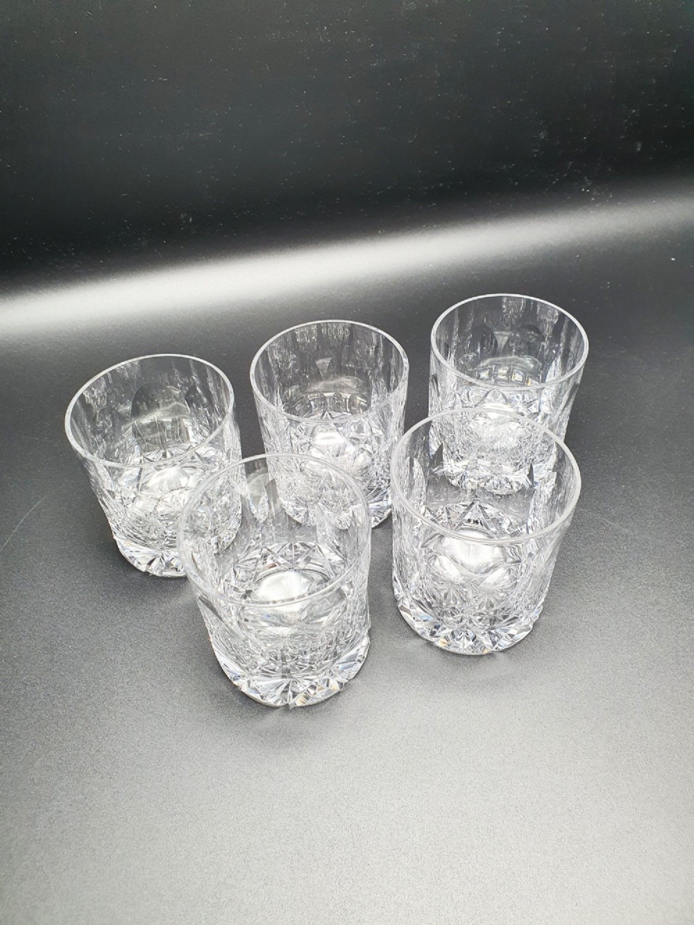 A set of five clear cut-glass tumblers featuring intricate geometric facet carvings around the lower half and base. View II