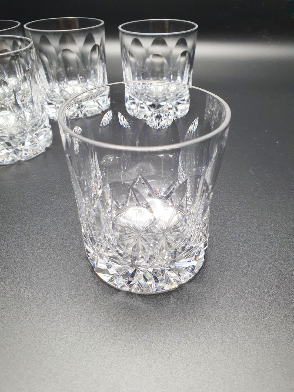 A set of five clear cut-glass tumblers featuring intricate geometric facet carvings around the lower half and base. View III