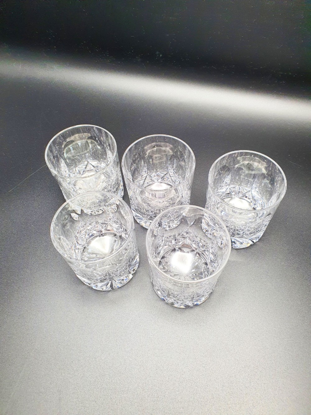 A set of five clear cut-glass tumblers featuring intricate geometric facet carvings around the lower half and base. View VI
