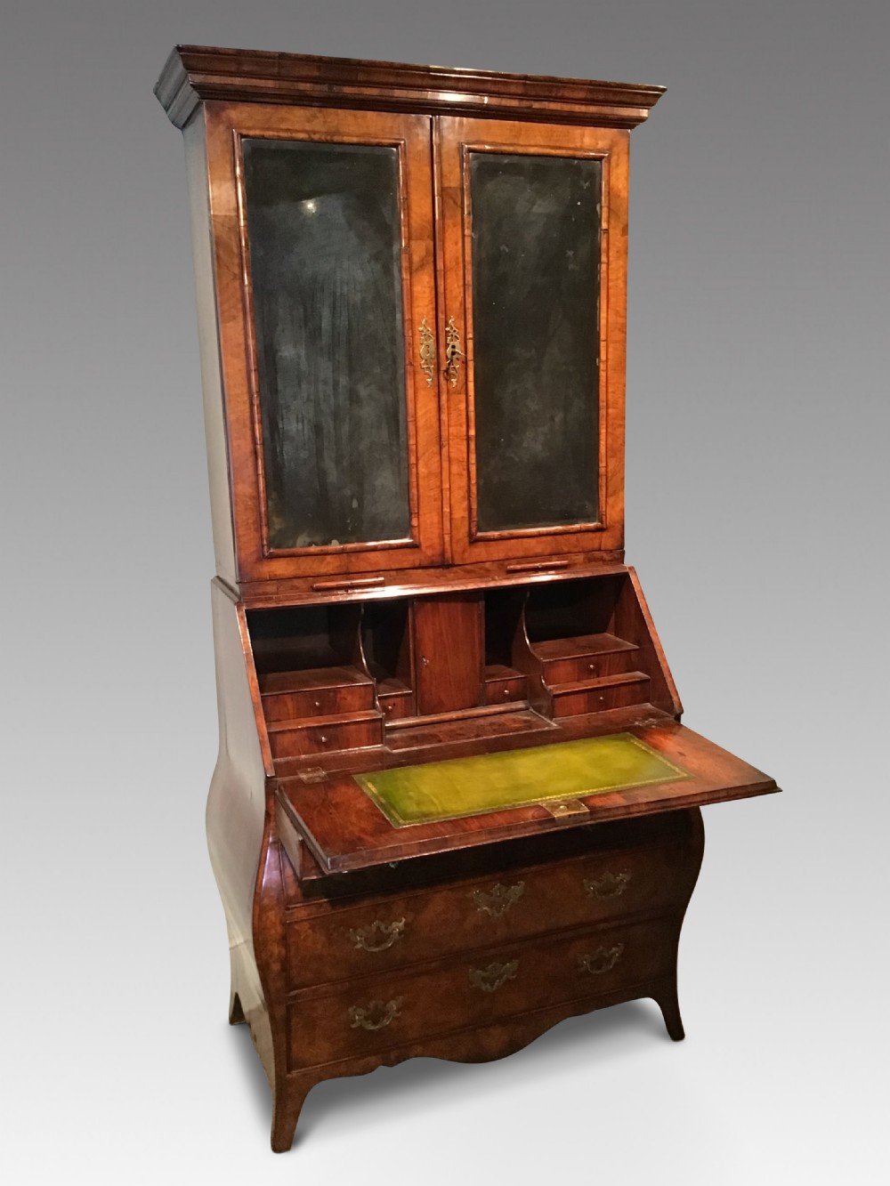 A two-part Georgian walnut bureau bookcase featuring a moulded top cabinet with two glazed doors above a fall-front desk with a green leather writing surface and a shaped lower drawer base.