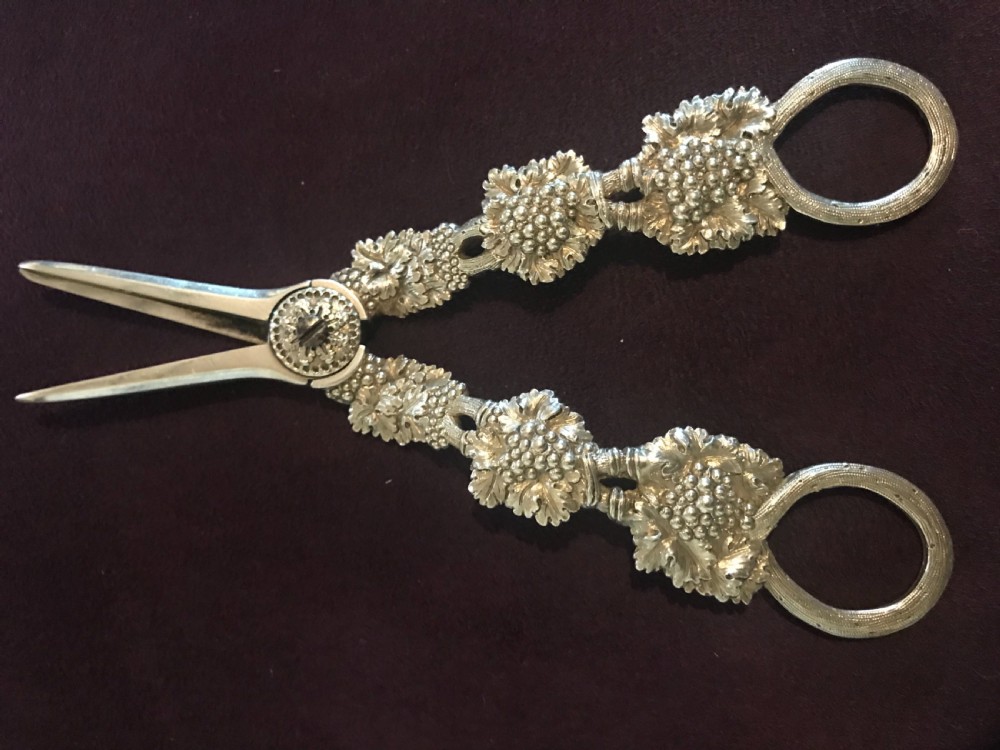 A pair of silver grape scissors featuring handles relief-moulded with grape clusters and vine leaves leading to round finger loops. View II