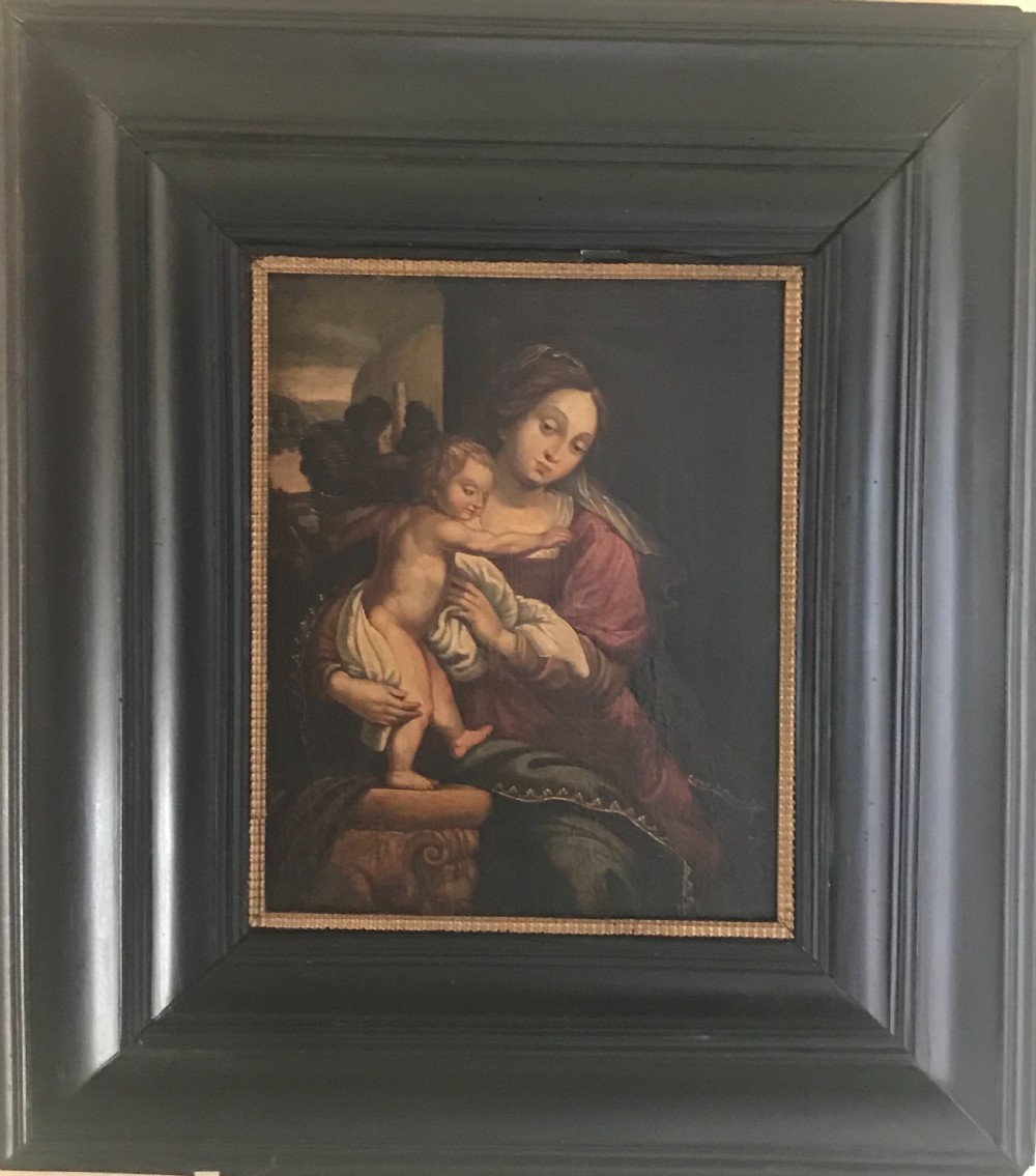 An antique oil painting depicting the Madonna in a burgundy dress holding the infant Christ, set within a heavy ebonised wooden moulding frame.