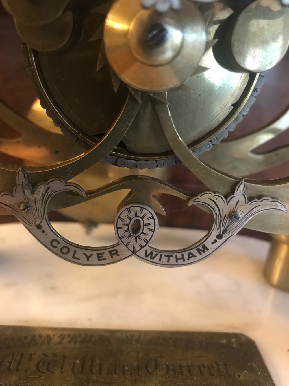 A Victorian brass skeleton clock with an exposed gear mechanism and silvered Roman numeral dial, encased in a clear glass dome on a white marble base. View III