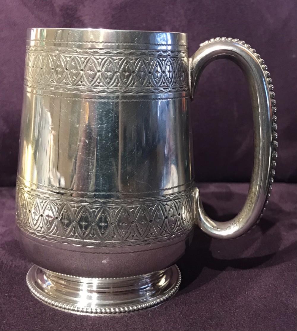 An antique sterling silver mug featuring engraved geometric borders, a beaded handle, and hallmarked stamps near the top rim. View II
