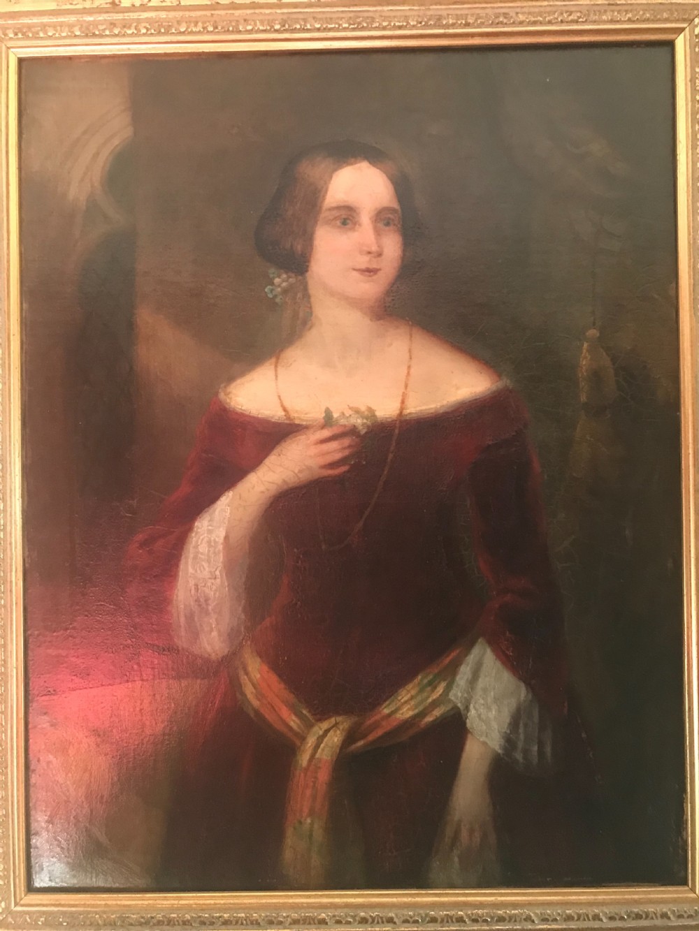 An antique oil painting on canvas depicting a woman in a deep red off-the-shoulder gown, enclosed within a wide gilded wooden frame. View II