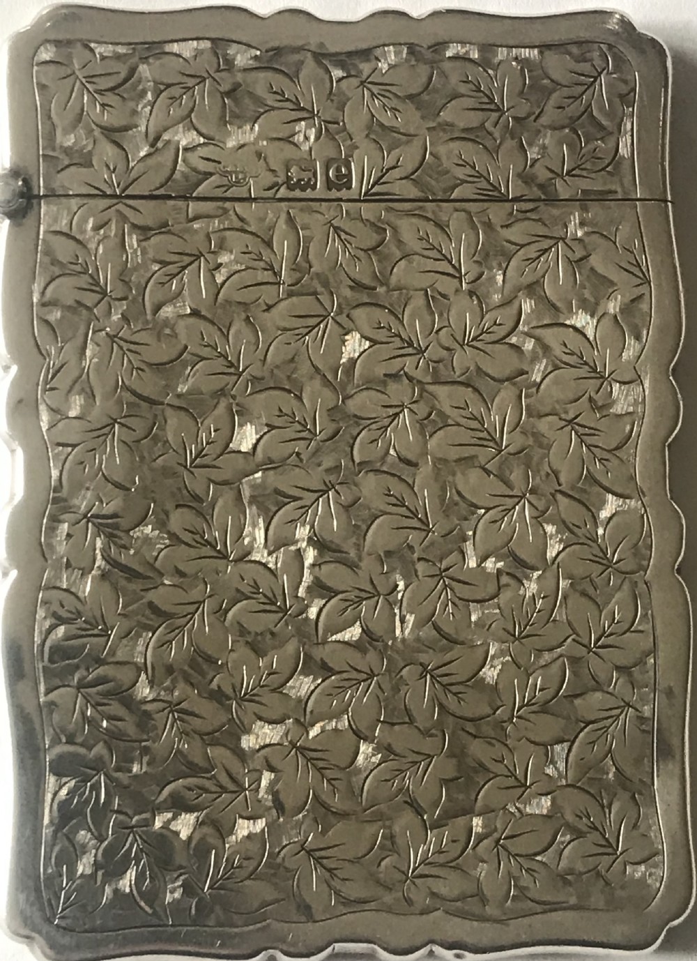 An antique silver card case featuring engraved leaf motifs, shaped scalloped edges, and a central circular cartouche. View II