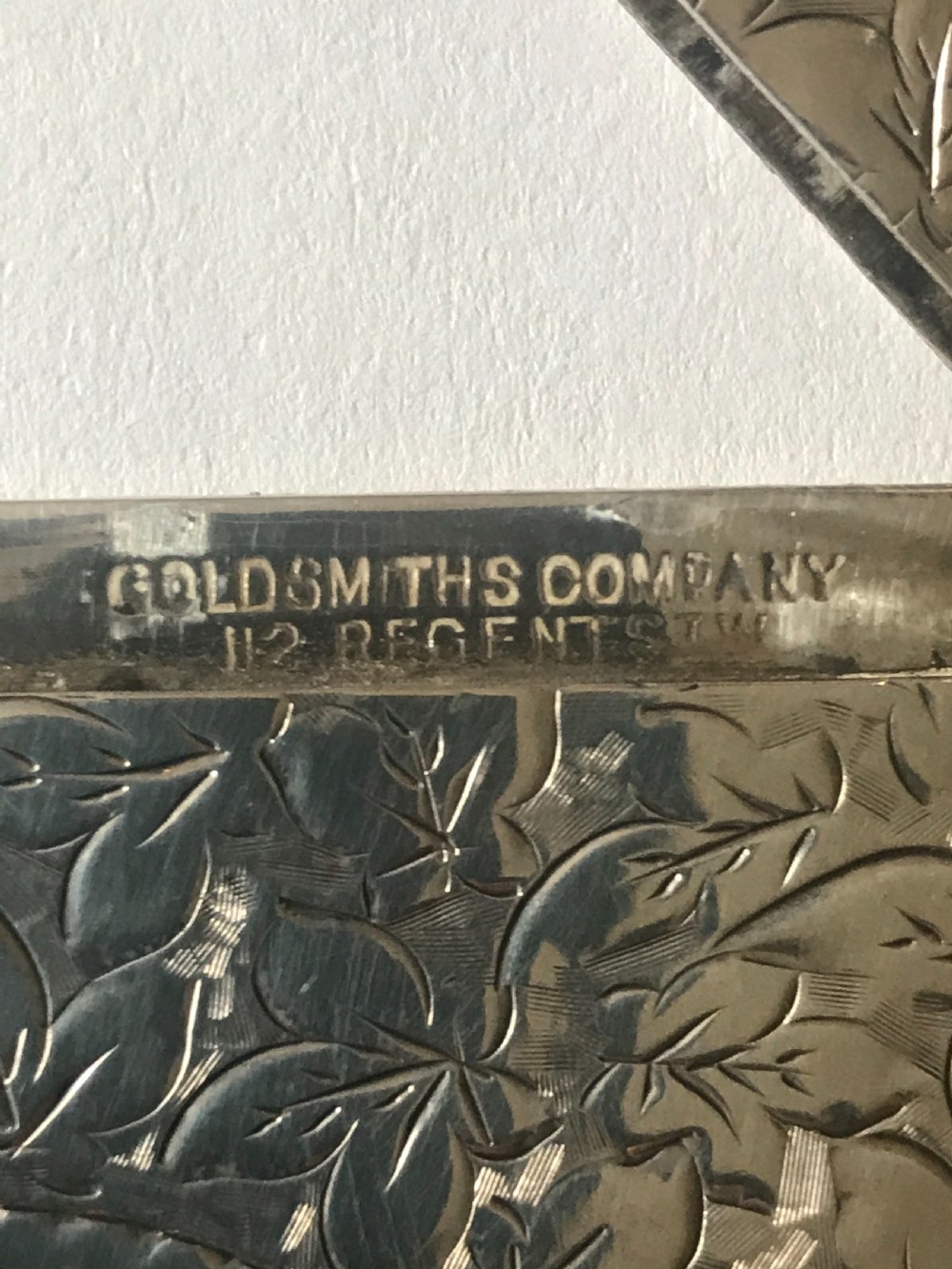 An antique silver card case featuring engraved leaf motifs, shaped scalloped edges, and a central circular cartouche. View IV