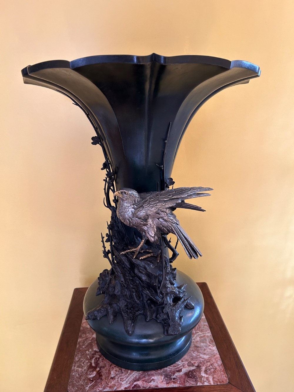 A dark patinated Japanese Meiji period bronze vase featuring a flared scalloped rim and a sculptural hawk perched on high-relief rockwork.